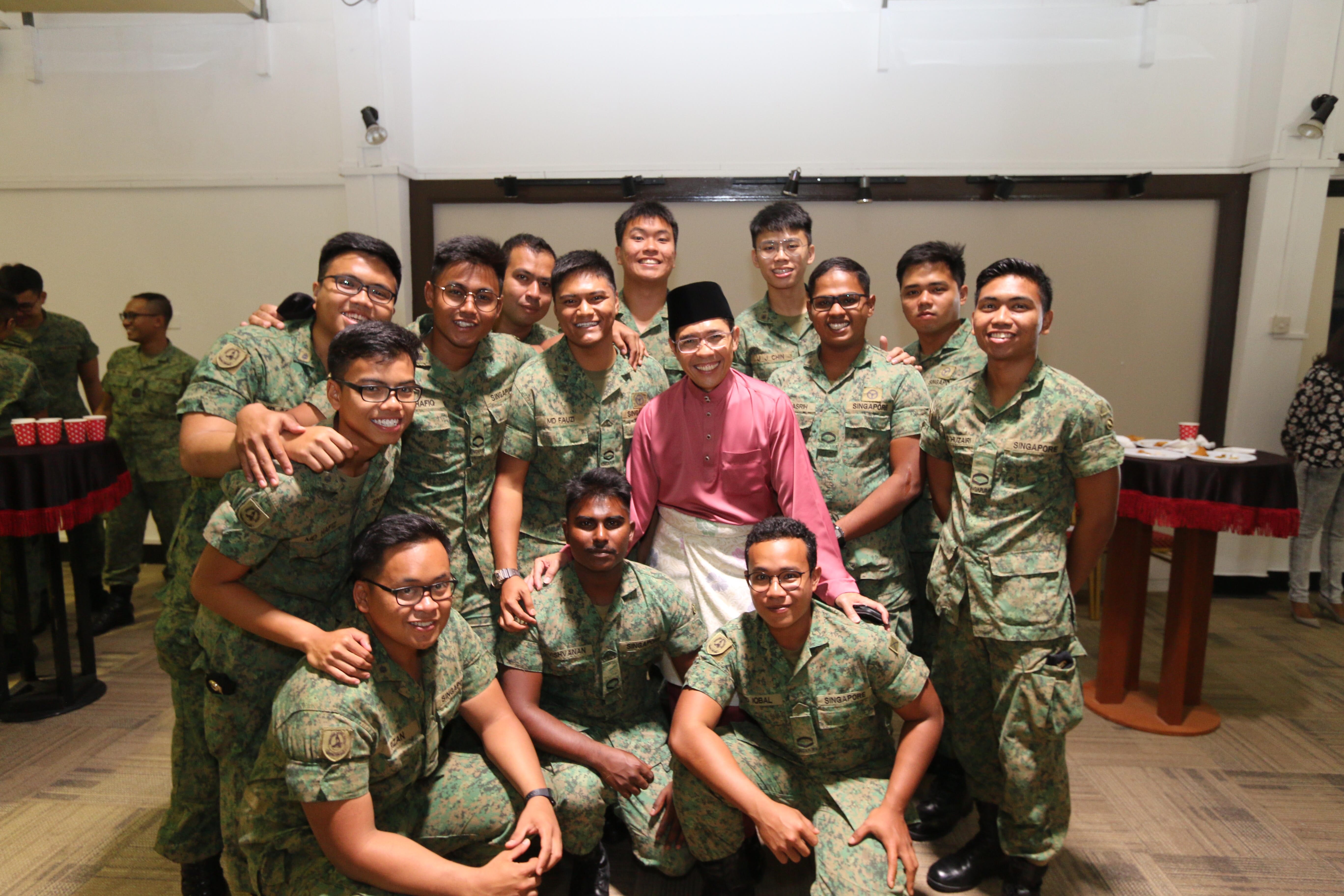 Group of people in Singapore military camouflage with a man in a pink shirt and sarong.